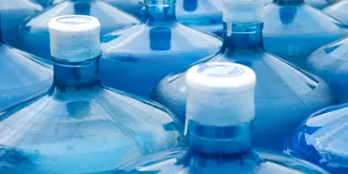 Close-up of multiple large blue water jugs with sealed caps, stored for emergency or bulk water supply.