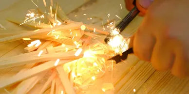 Close-up of hands using a ferro rod to spark a fire over kindling.