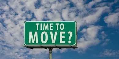Green road sign with the words "TIME TO MOVE?" against a blue sky with scattered clouds.