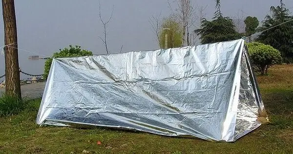 Emergency A-frame shelter made from a reflective mylar blanket tied between two trees.