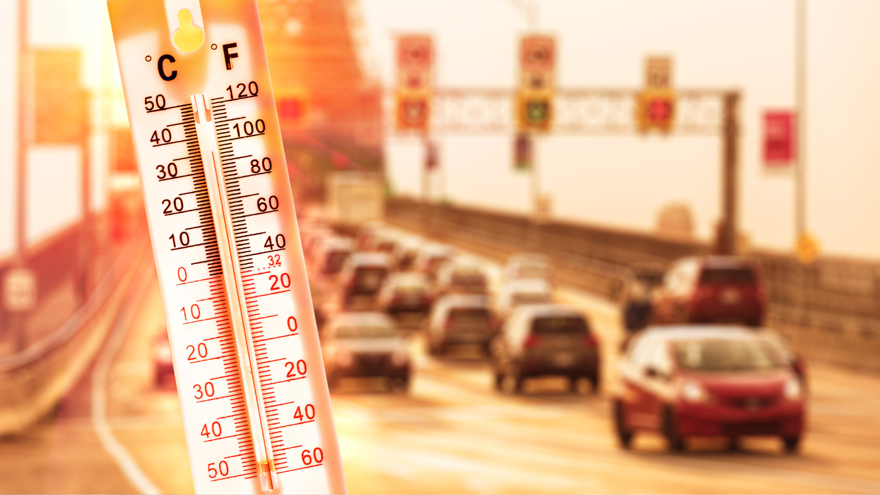 Extreme heat preparedness. Thermometer showing high temperatures with blurred traffic in the background on a sun-heated city road.