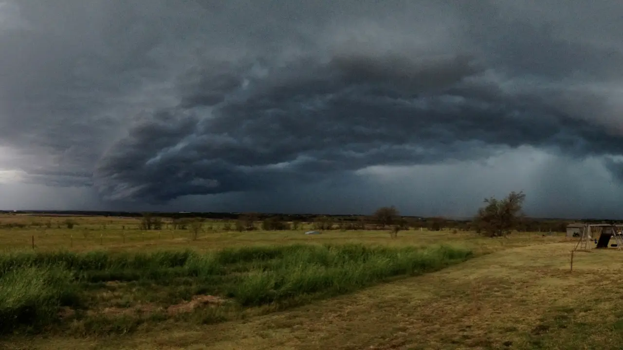 Dark storm clouds forming over a rural landscape, signaling an approaching tornado.