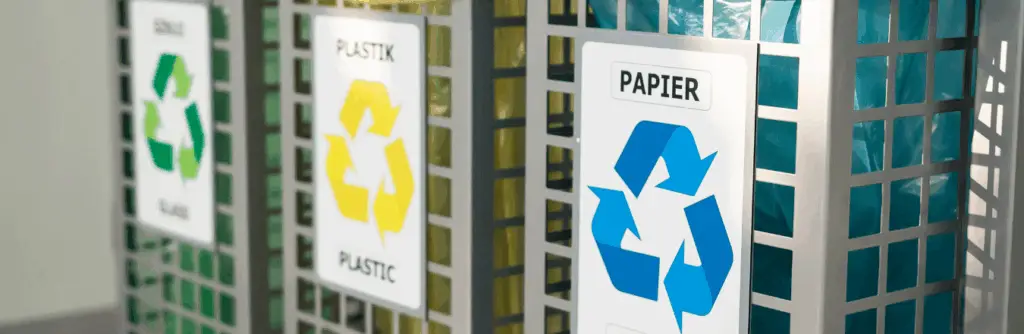 Three metal recycling bins labeled for glass, plastic, and paper, each with color-coded bags and recycling symbols.